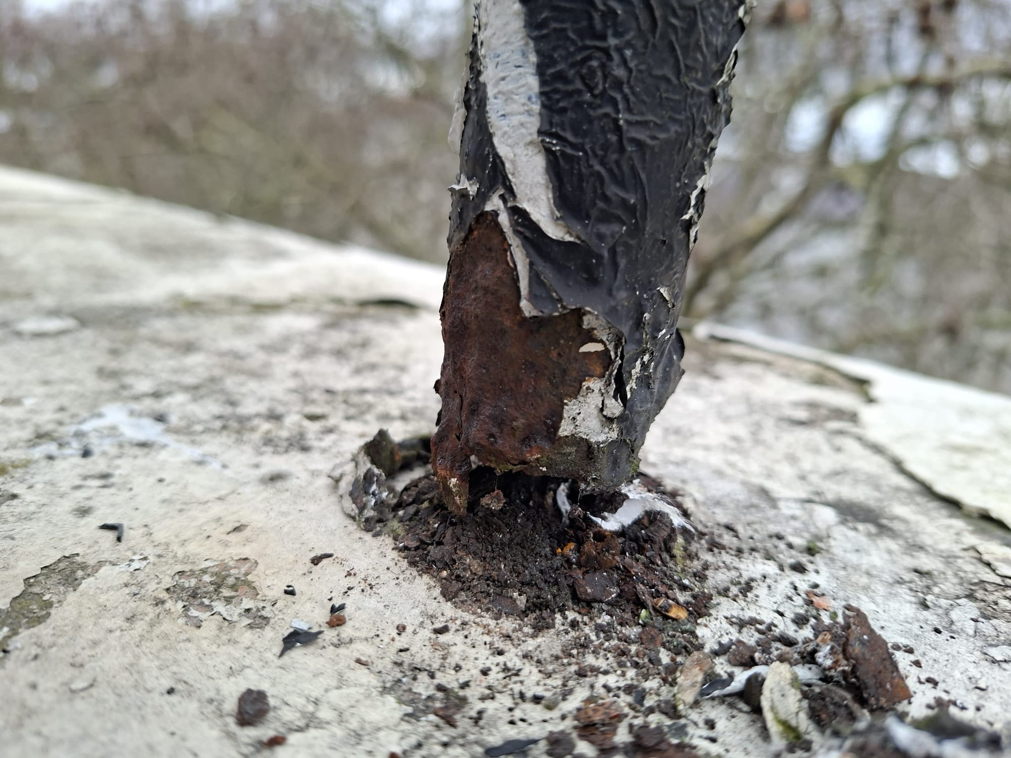 Corroded guardrail post with peeling coating on a rooftop, showing equipment in need of repair