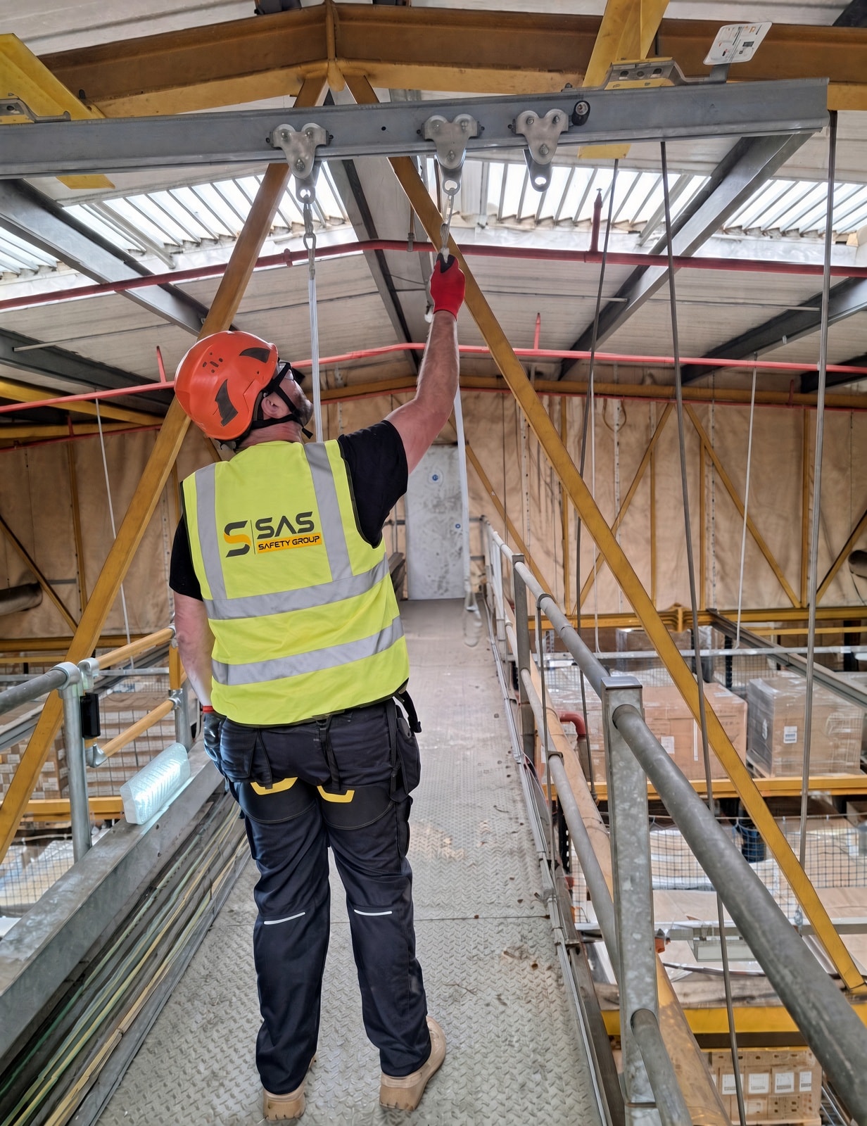 SAS Safety Group technician inspecting fall-arrest anchor points on a warehouse walkway
